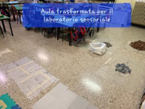 foto dell'aula trasformata in percorso sensoriale: percorso con ciottoli, foglie, tessuto, bolle di plastica...